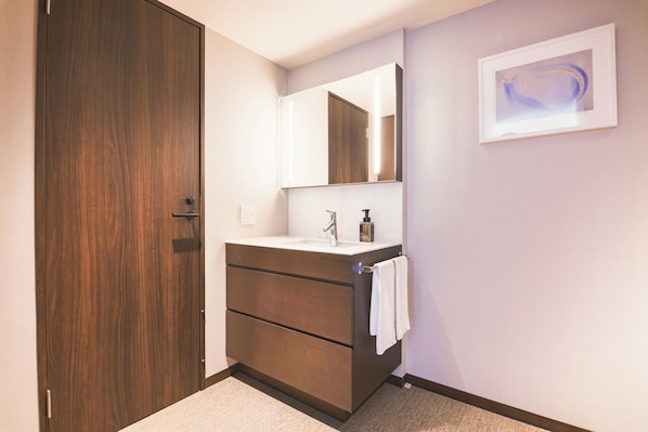 A bathroom with a wooden door, a sink with a mirror, and a framed artwork on the wall.