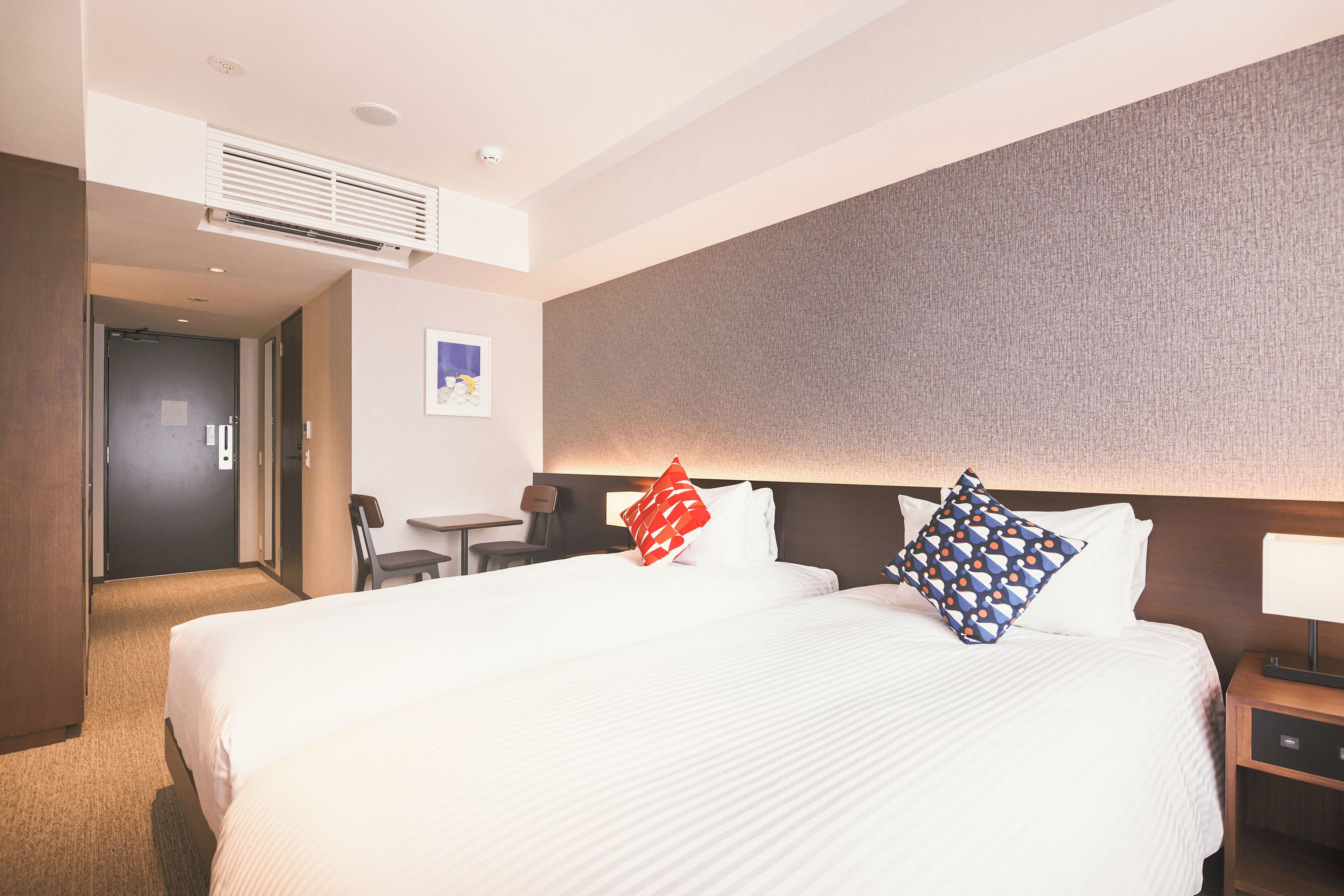 A hotel room with a large bed, a desk, a chair, and a wall-mounted air conditioner.