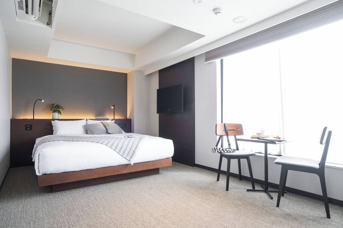 A modern hotel room with a large bed, a desk, and a TV.