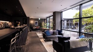 Un bar moderno con una barra larga y taburetes, un área de estar con sofás y sillones, y grandes ventanales con vistas al exterior.