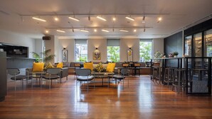 Un hall espacioso con suelo de madera, zona de estar con sofás y sillones, y una zona de bar con taburetes.