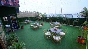 An outdoor patio with tables and chairs, surrounded by potted plants and a wooden fence. - HOTEL JAI HARSH BY DIVYANSHI HOSPITALITY (Jaipur)