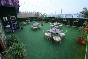 An outdoor patio with tables and chairs, a washroom, and a view of the city. - HOTEL JAI HARSH BY DIVYANSHI HOSPITALITY (Jaipur)