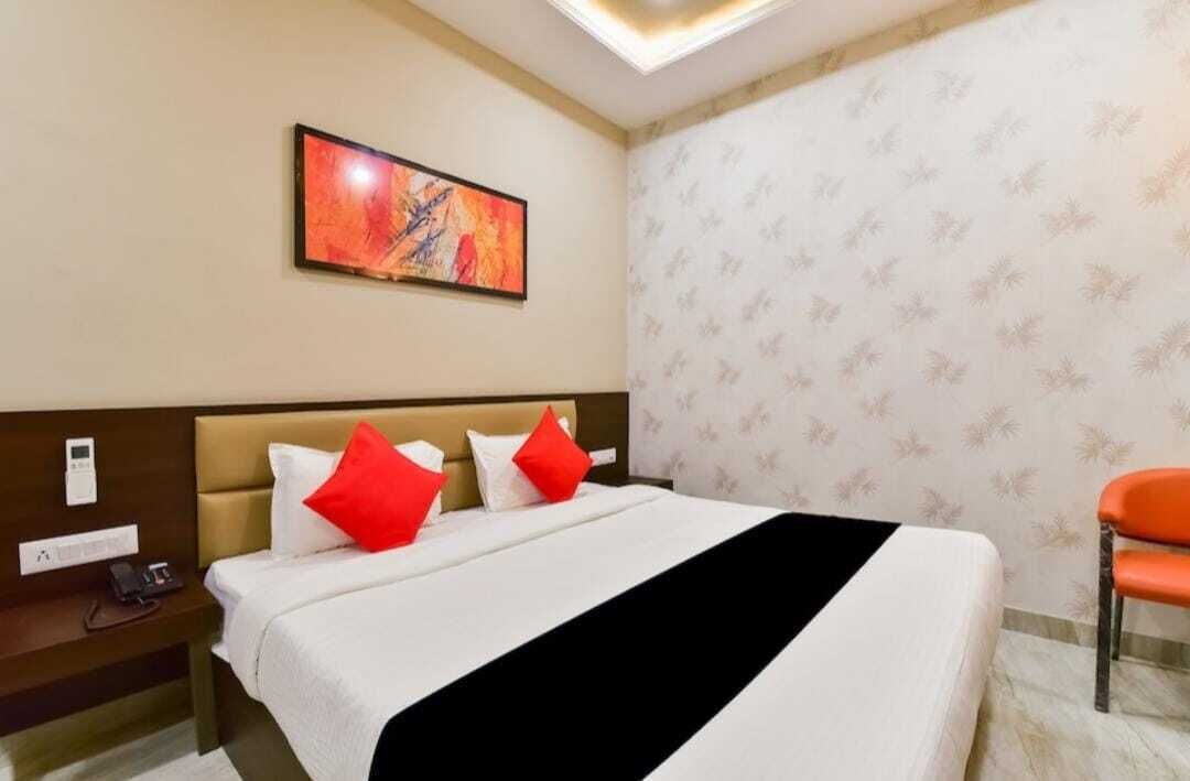 Una habitación de hotel con cama, mesita de noche con teléfono, un cuadro en la pared y papel tapiz estampado.