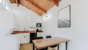 Cocina compacta con alacenas blancas, techo de madera, microondas y una mesa de comedor con sillas.