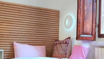 Un dormitorio con cabecera de madera, cama con ropa de cama rosa, espejo redondo y armario de madera.