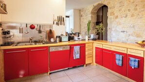 A kitchen with red cabinets, a stone wall, and various kitchen appliances. - Maison Entière Haut Valromey (HAUT-VALROMEY)