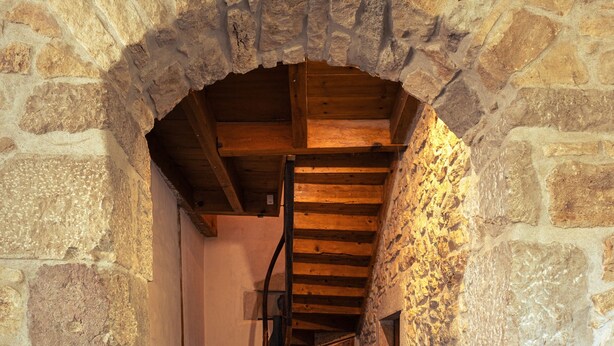 A stone-walled corridor with a wooden staircase leading to a door. - Maison Entière Haut Valromey (HAUT-VALROMEY)