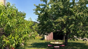 A grassy yard with a wooden table and chairs, a shed, and a tree. - Maison Entière Haut Valromey (HAUT-VALROMEY)