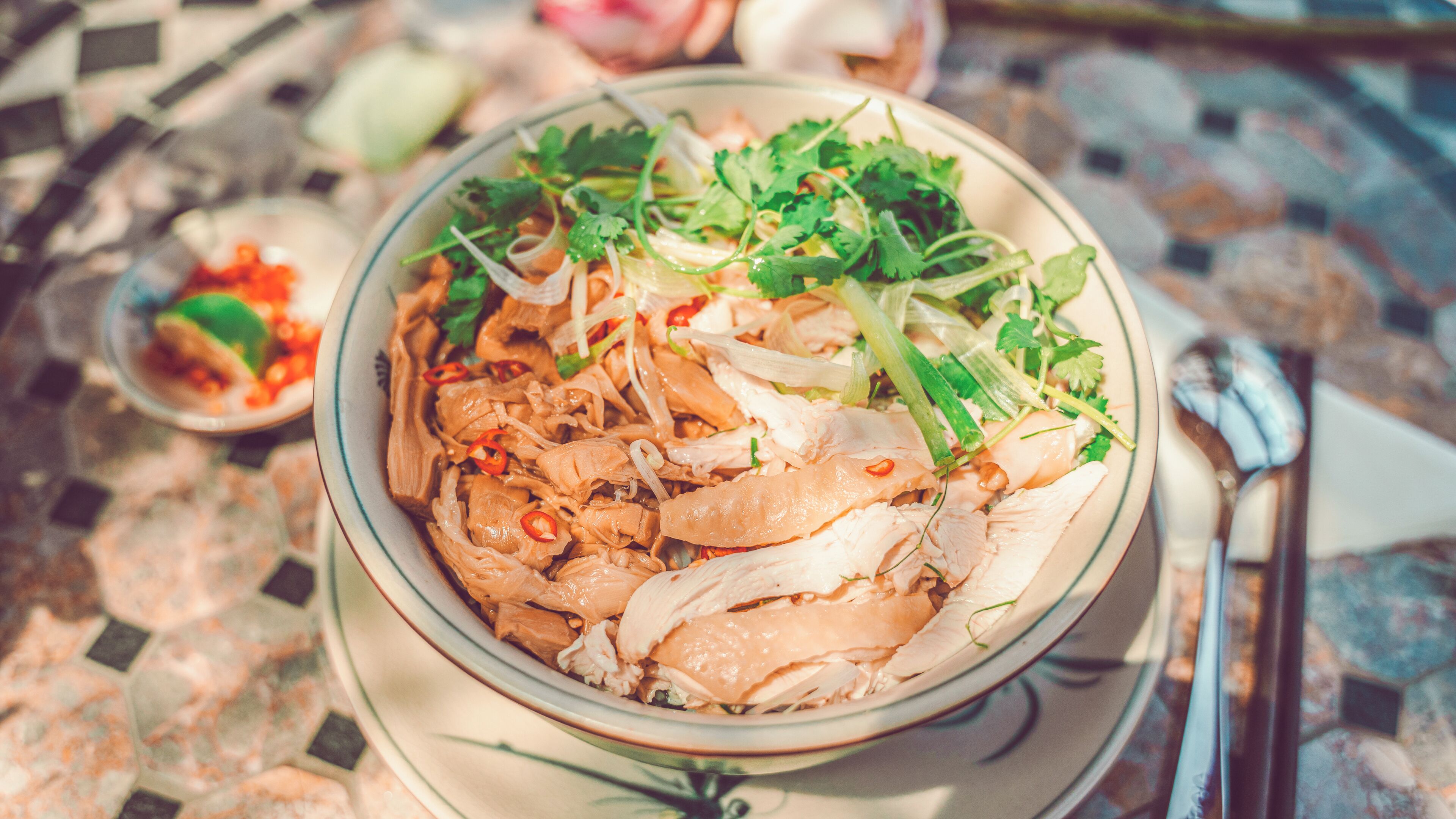 A bowl of food with various ingredients, including shredded meat and vegetables, on a table with a tiled floor.