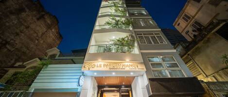 Un hôtel à la façade moderne, une enseigne indiquant « Le Parfum Hanoi », et une entrée bien visible avec un escalier menant à la porte.