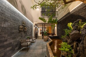 A narrow indoor corridor with a stone wall, a small water feature, wicker chairs, and potted plants. - Le Parfum Apartment And Hotel (Hanoi)