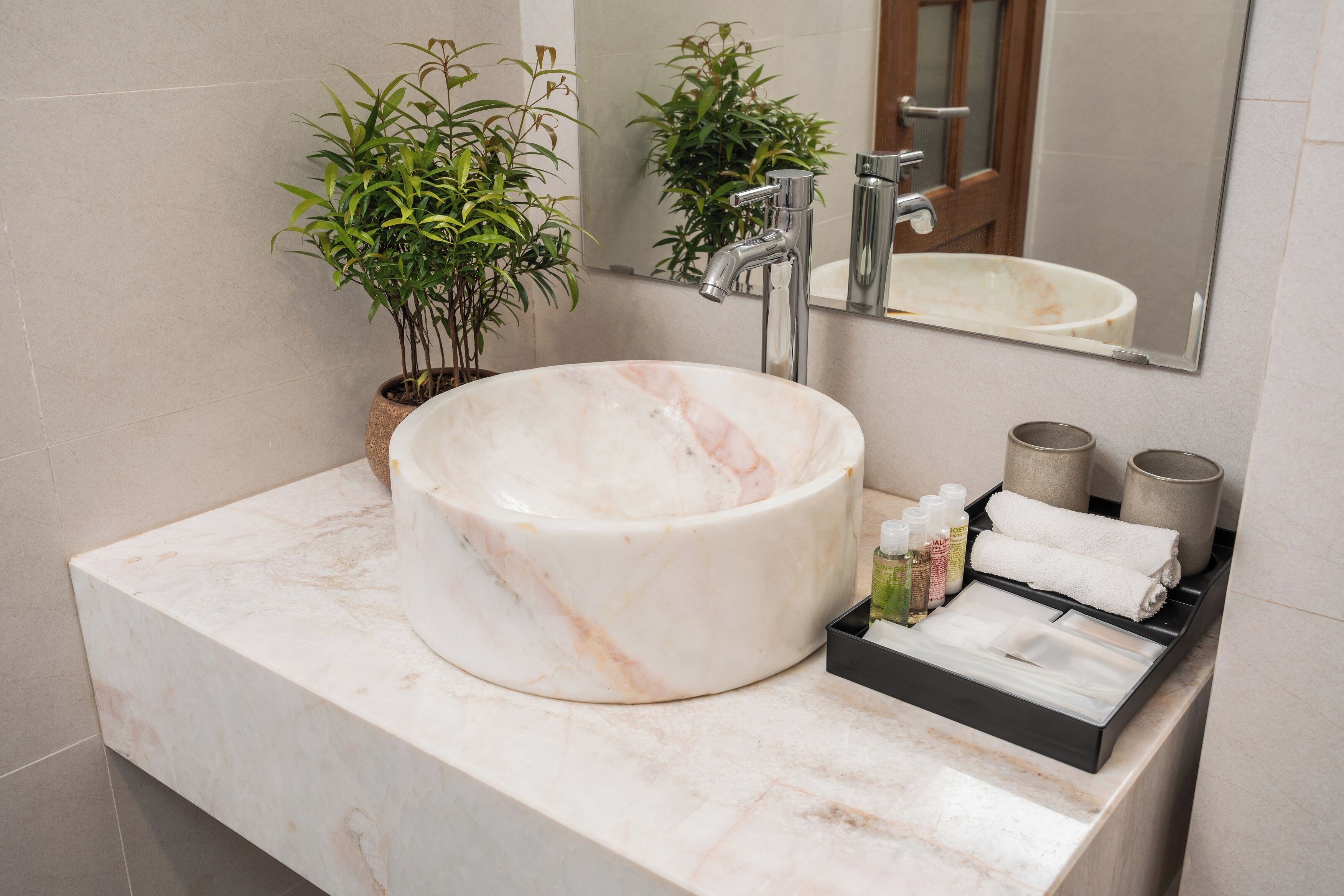 A bathroom with a large marble sink, a mirror, a potted plant, and toiletries.