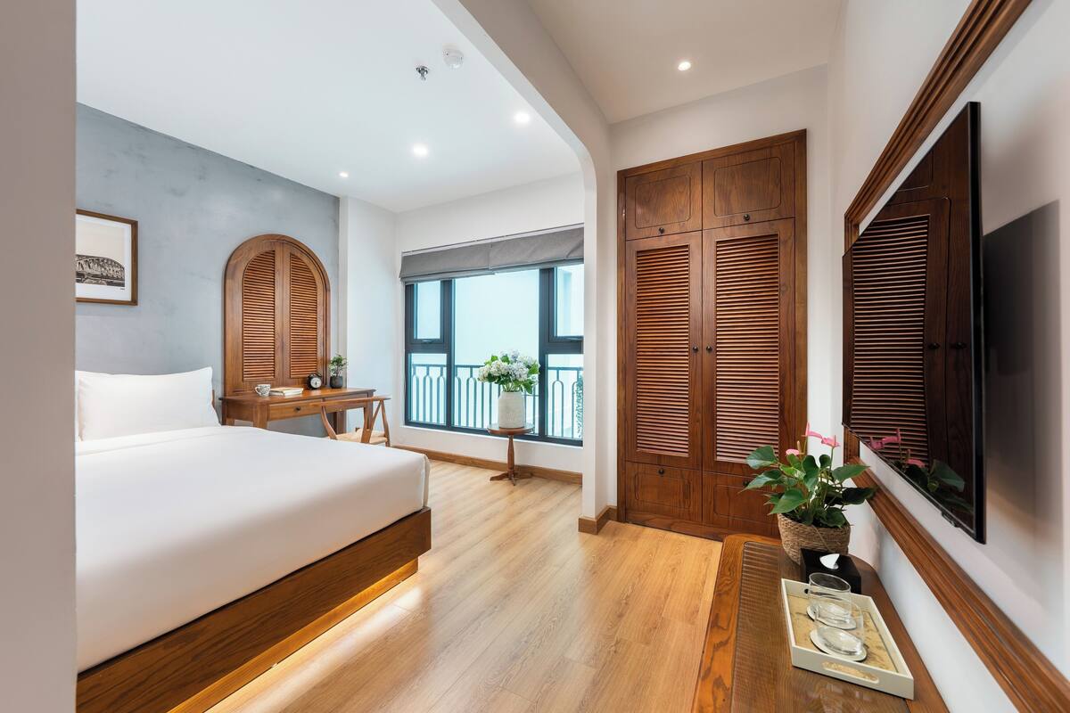 Une chambre avec un lit, une armoire en bois, une télévision et un balcon avec vue.