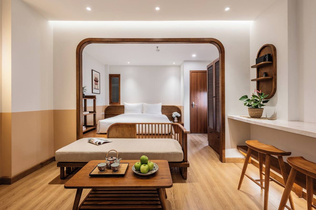 Une chambre d’hôtel avec un lit, une table de chevet, un petit coin salon et un plancher en bois.