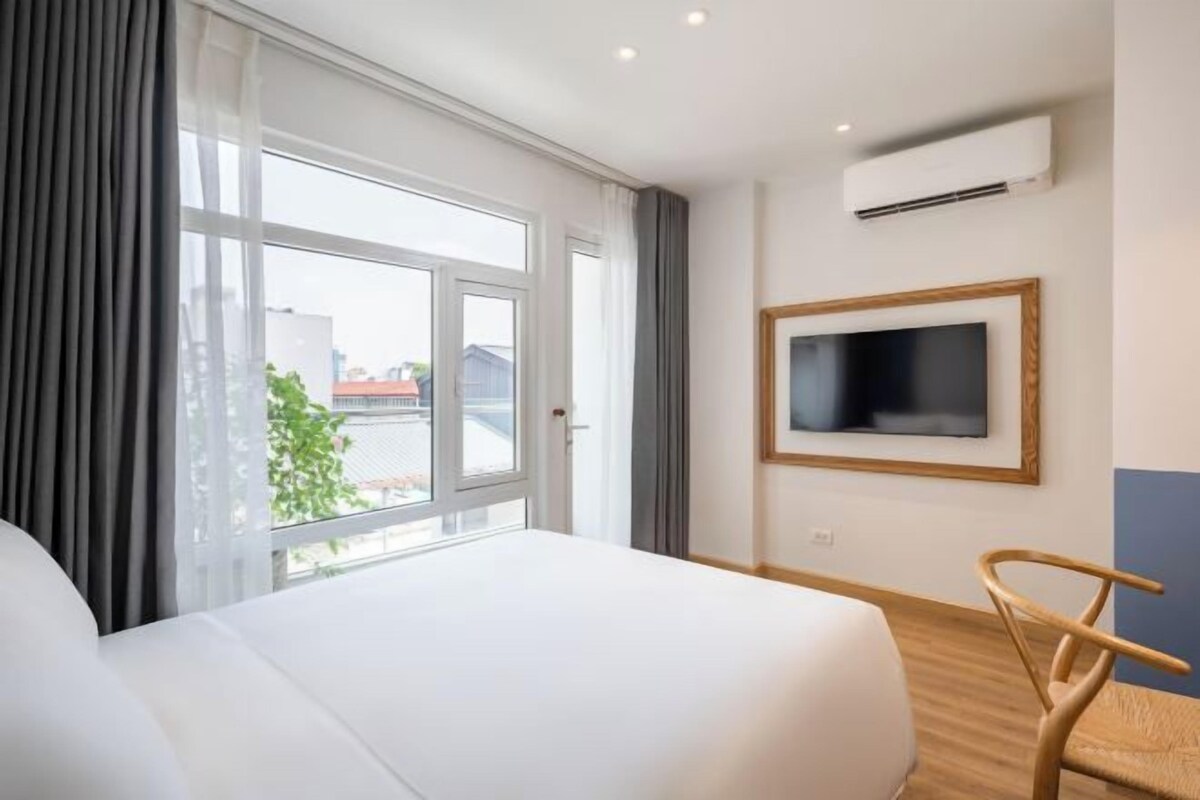 A hotel room with a large bed, a television mounted on the wall, and a window with curtains.