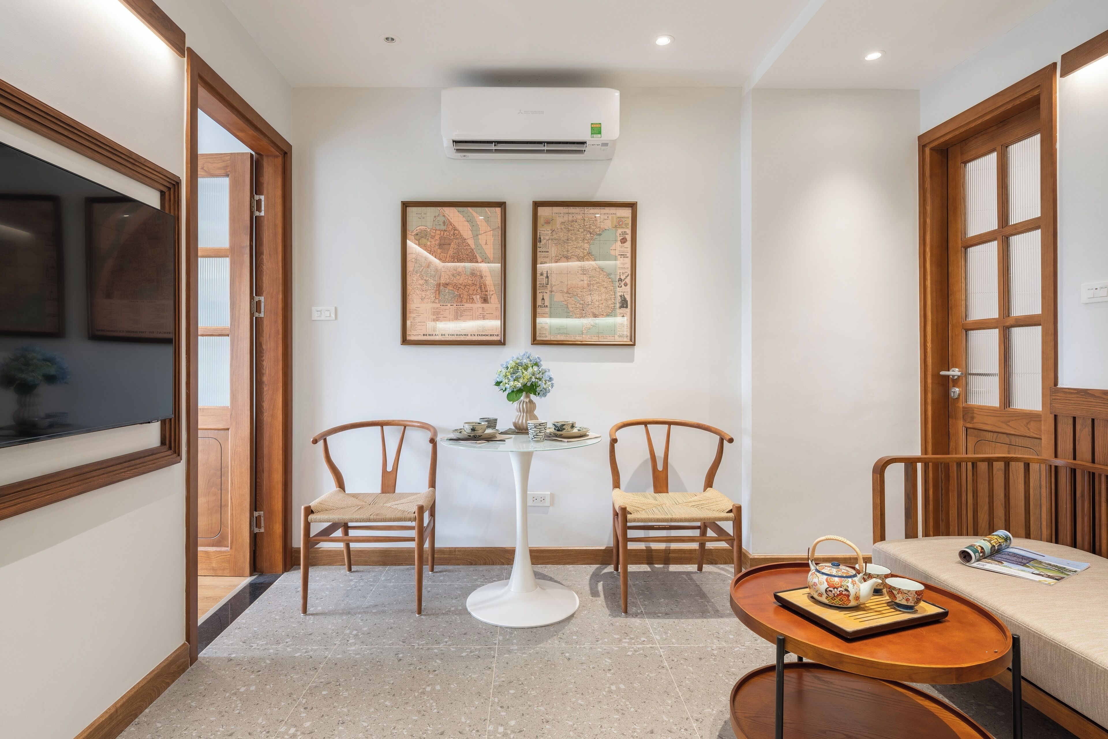 A hallway with a round table, two chairs, a small table with a vase, and framed maps on the wall.