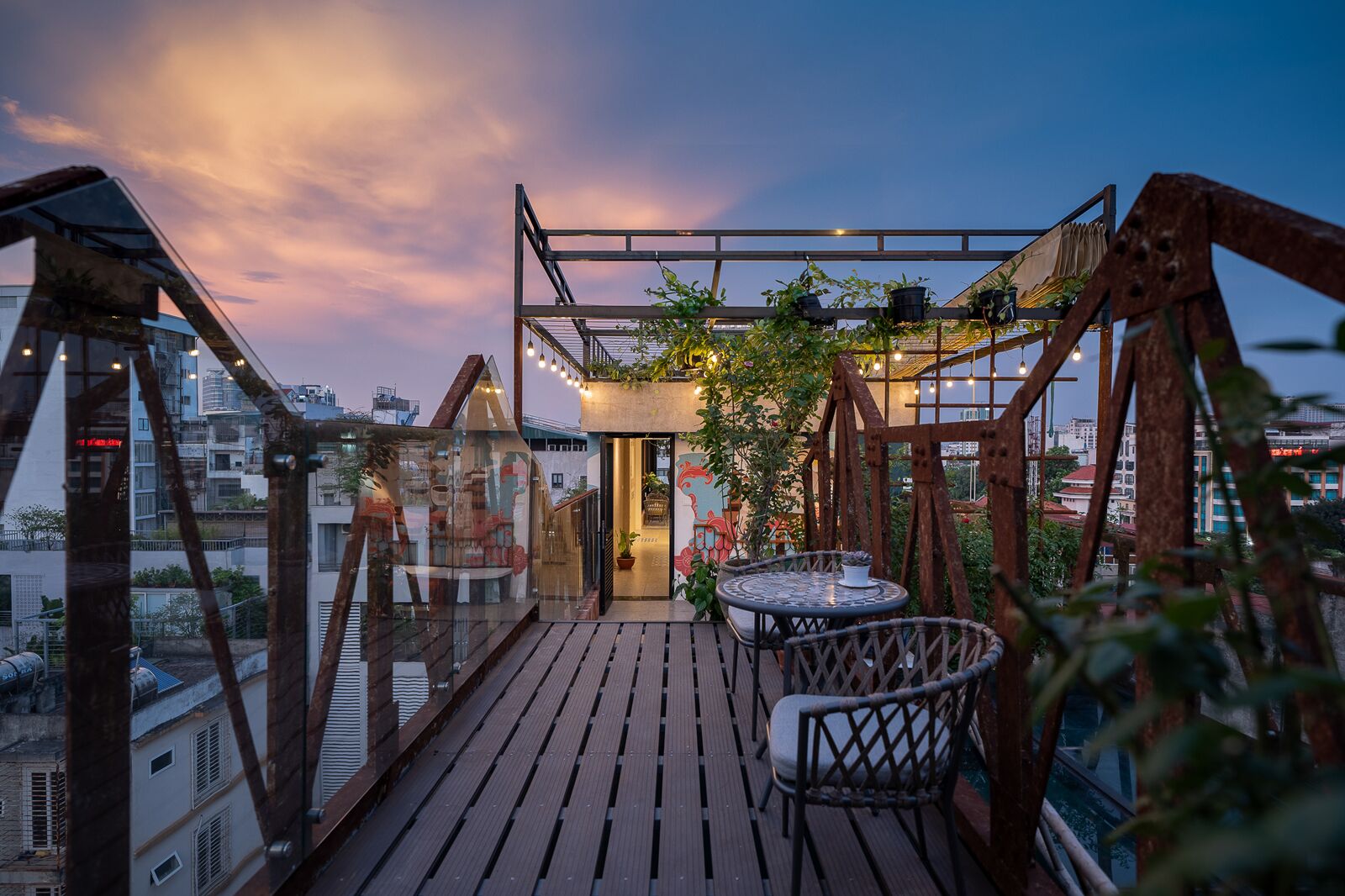 A rooftop terrace with a wooden deck, a round table with chairs, and a view of the cityscape.
