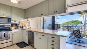 A modern kitchen with a dishwasher, microwave, and stove. There is a large window overlooking a balcony with outdoor seating.
