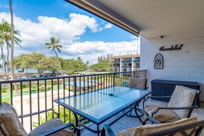 A balcony with a glass table and chairs, overlooking a parking lot and a pool area.