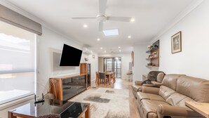 A modern living room with a sofa, TV, and dining area. - Highett Charm - 3 bedroom Unit (Highett)