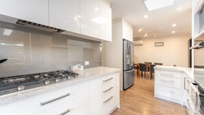 A modern kitchen with white cabinetry, stainless steel appliances, and a wooden floor. - Highett Charm - 3 bedroom Unit (Highett)
