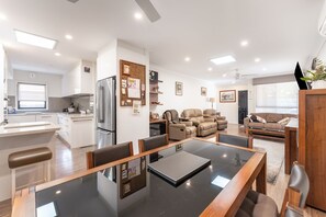 A modern kitchen with a refrigerator, a dining table with chairs, a sofa, and a coffee table in a living area. - Highett Charm - 3 bedroom Unit (Highett)