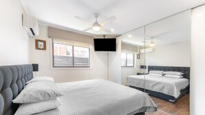 A modern bedroom with a large bed, a ceiling fan, a flat-screen TV, and a large mirror. - Highett Charm - 3 bedroom Unit (Highett)
