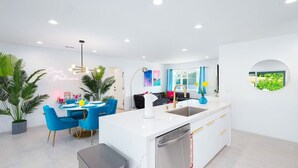 Una cocina moderna con armarios blancos, lavavajillas de acero inoxidable y una zona de comedor azul con sillas a juego.