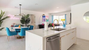 Una cocina moderna con una isla central, armarios blancos y lavavajillas de acero inoxidable.
