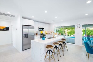Een moderne keuken met een centraal eiland, roestvrijstalen apparatuur en uitzicht op een buitenzwembad.
