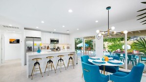 Una cocina moderna con armarios blancos, una isla central con taburetes y un área de comedor con sillas azules y una mesa redonda.
