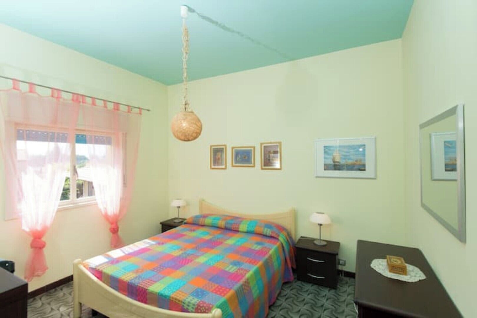 A bedroom with a bed, bedside tables, a hanging lamp, and a window with curtains.