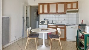 Une cuisine compacte avec des meubles en bois, une cuisinière blanche et une petite table à manger avec deux chaises.