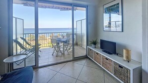 Un balcon avec vue sur la mer, une table à manger, des chaises, un canapé, un téléviseur et une plante décorative.