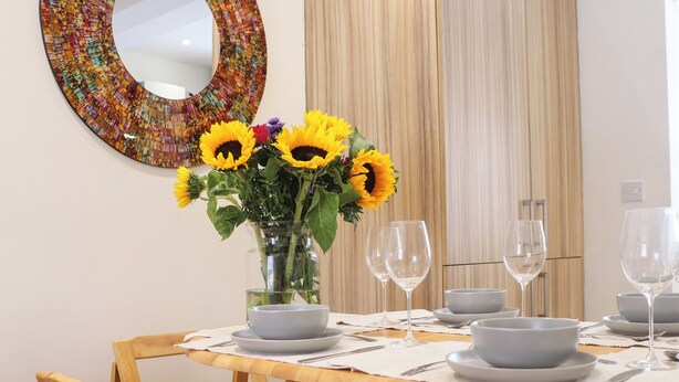 A dining table set with white plates, bowls, and wine glasses, surrounded by wooden chairs. - 4 Martindales Yard (Kendal)