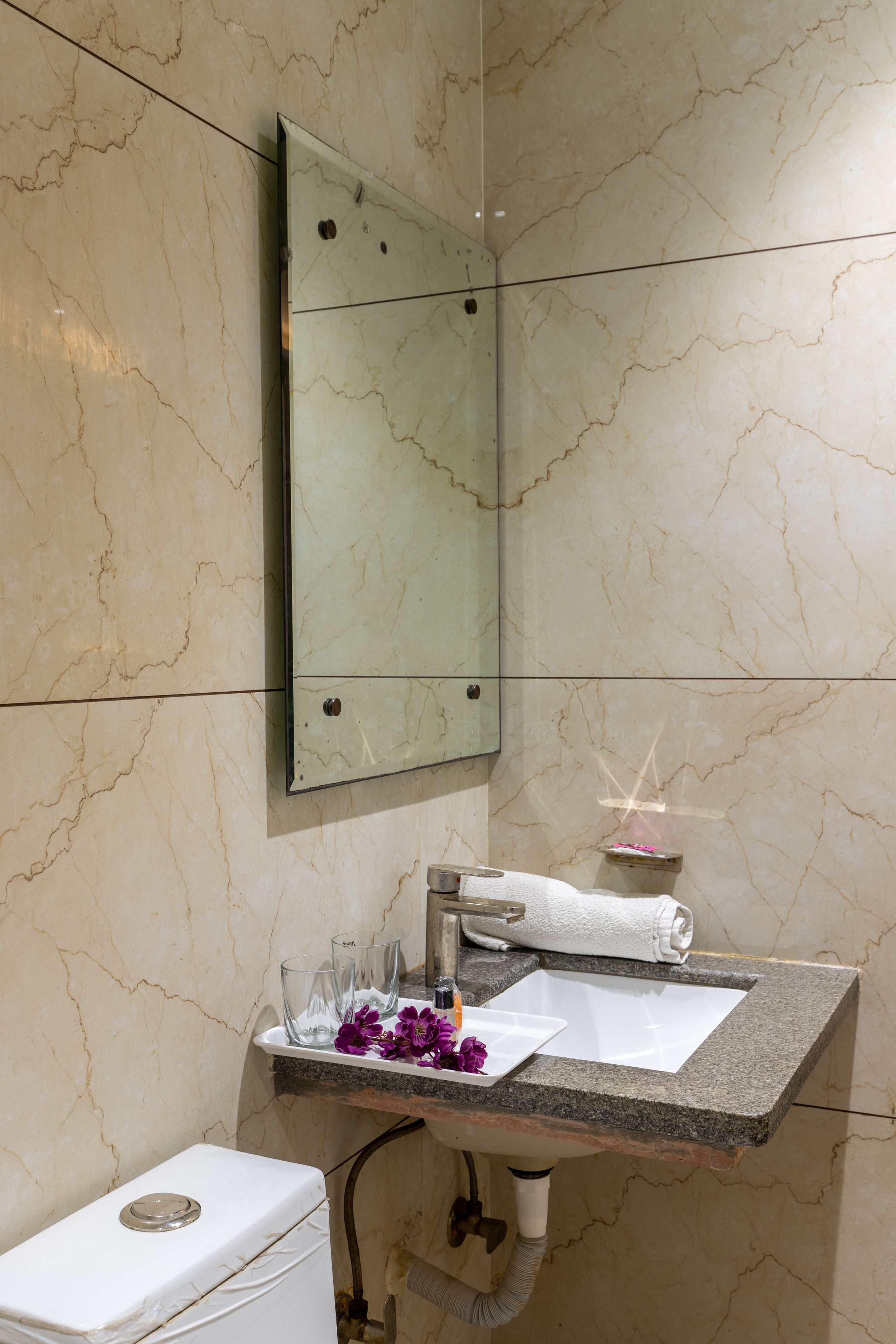 Un baño con pared de mármol, un lavamanos con una toalla y un inodoro.