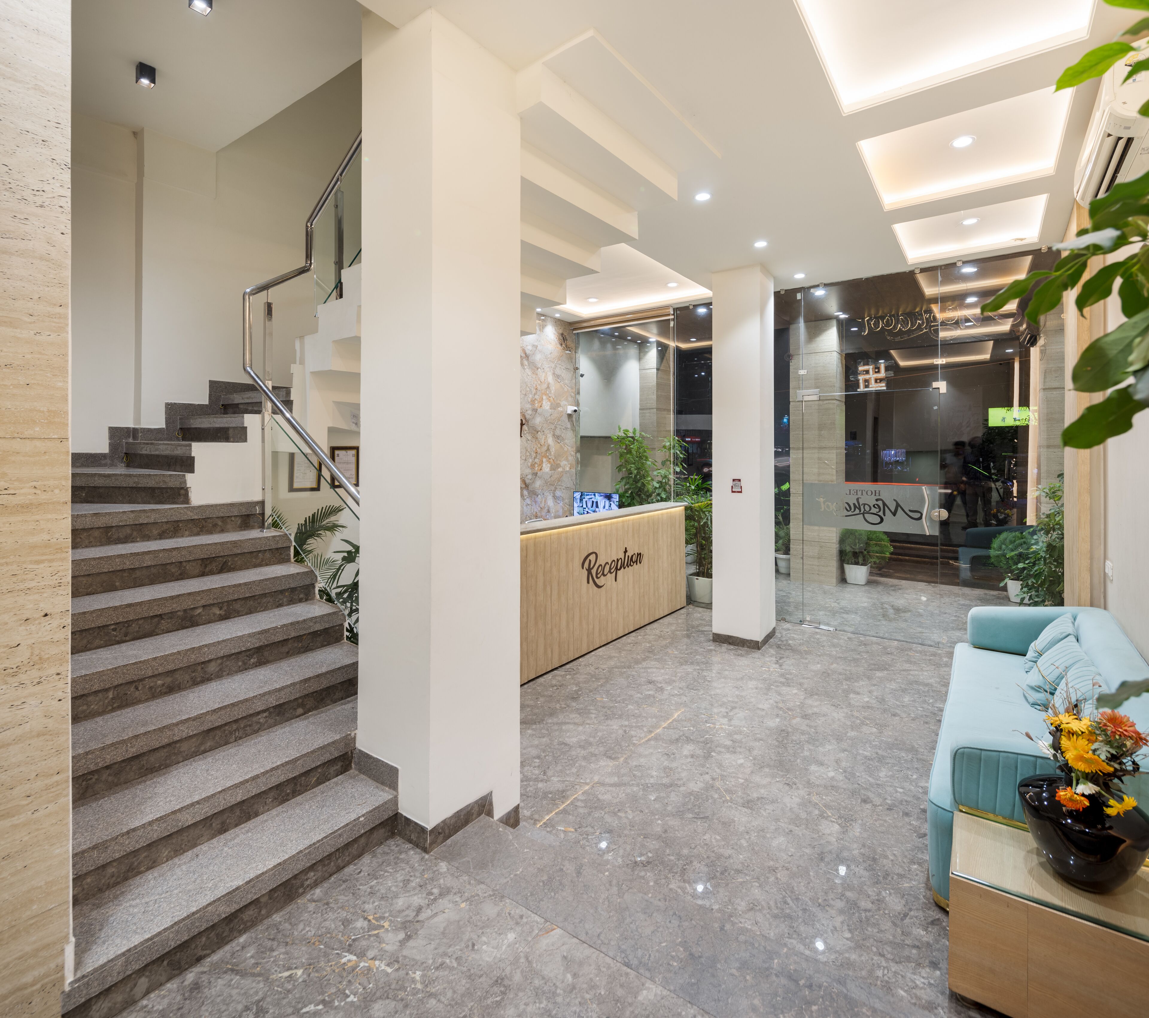 A modern reception area with a marble reception desk, a staircase with metal railings, and a blue sofa with a vase of flowers.
