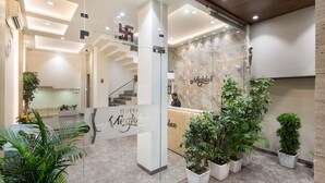 Zona de recepción de un hotel con diseño moderno, que incluye un mostrador de mármol, una escalera y plantas en macetas.