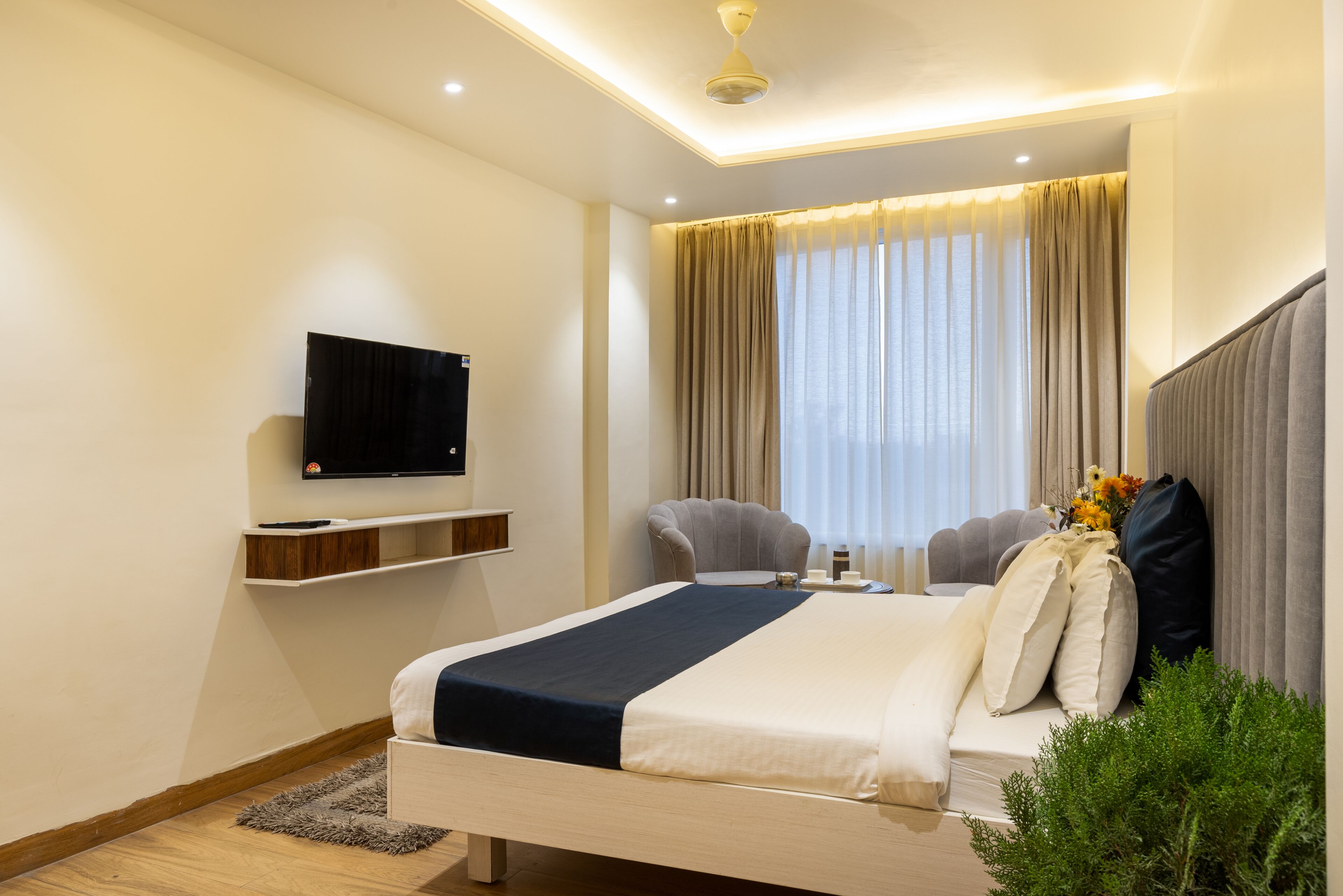 Una habitación de hotel moderna con una cama, un televisor montado en la pared, una mesita pequeña y una silla.