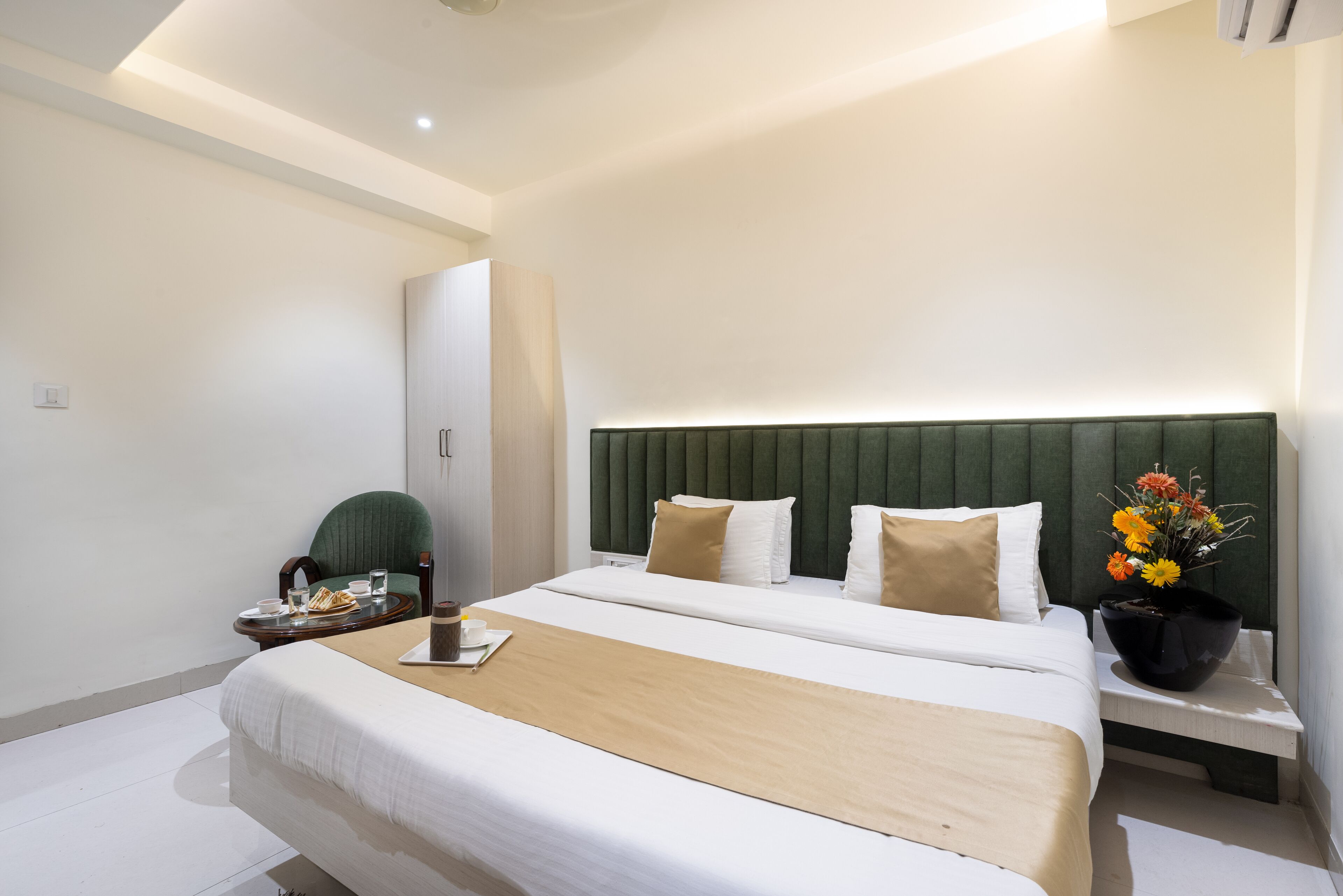 A modern hotel room with a large bed, a bedside table with a lamp, and a small table with a tray of breakfast items.
