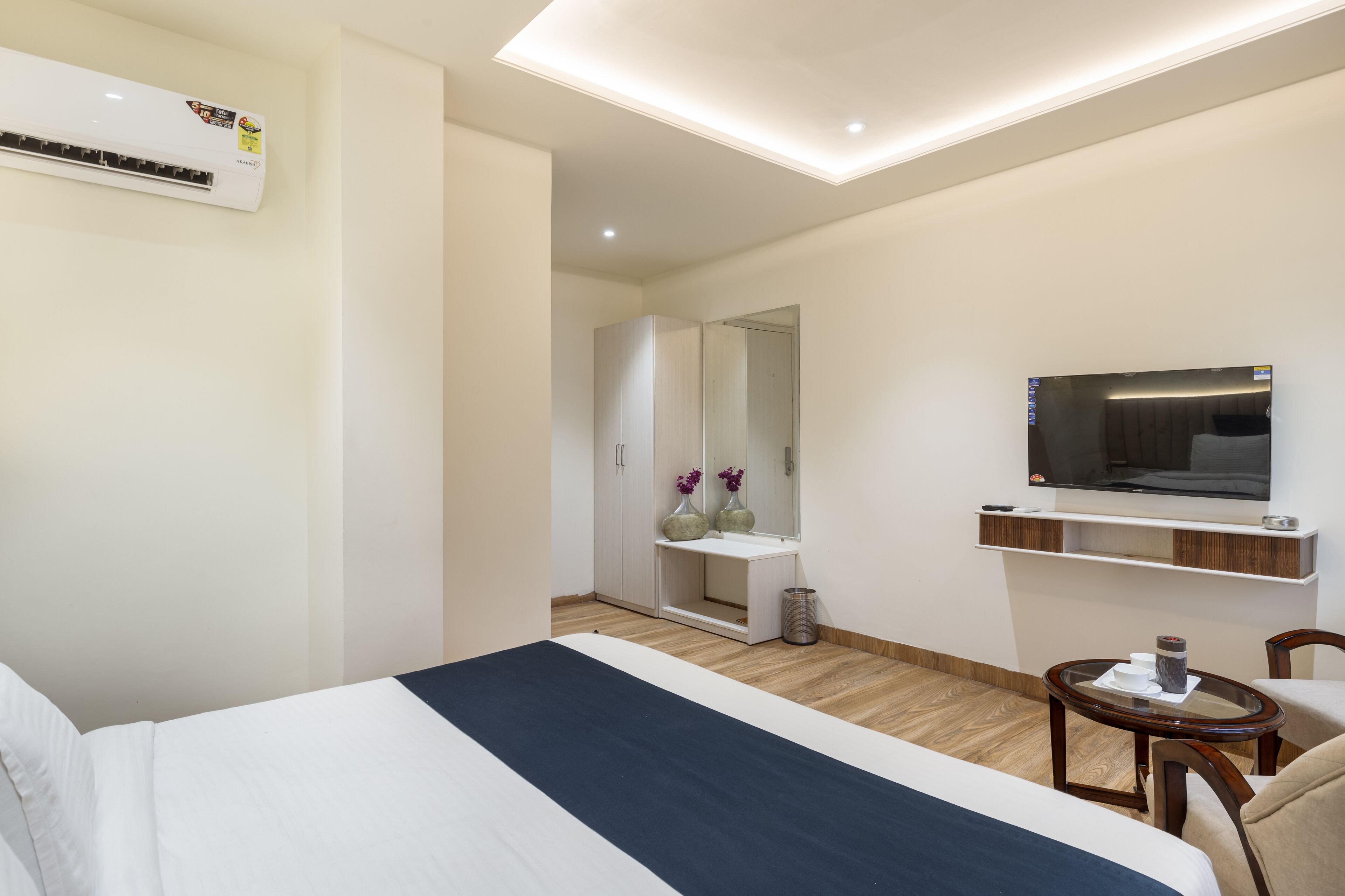 A modern hotel room with a large bed, a TV, a small table, and a mirror.