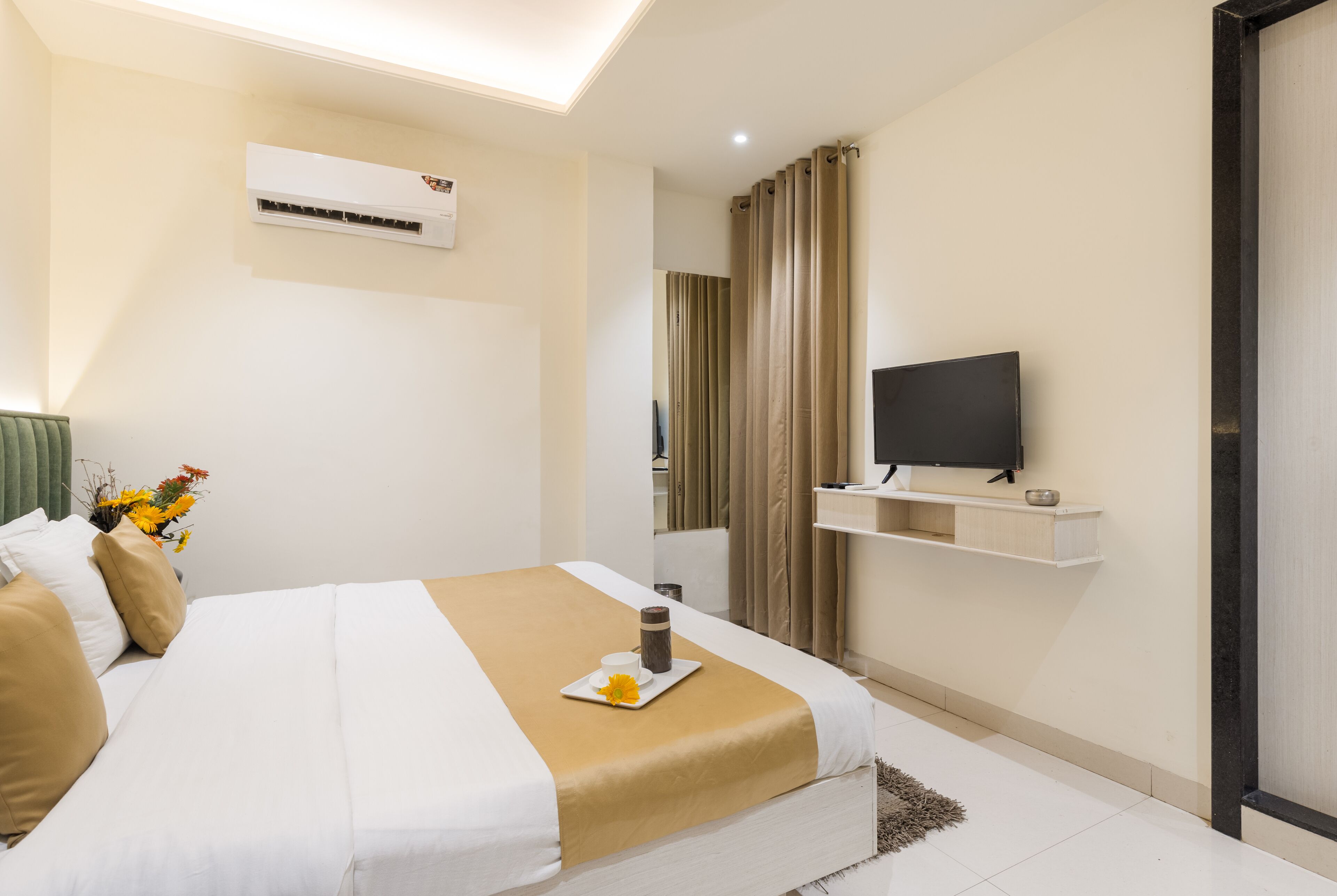 Une chambre d’hôtel moderne équipée d’un lit, d’un téléviseur fixé au mur, d’un climatiseur et d’une petite étagère sur laquelle se trouve une télécommande.