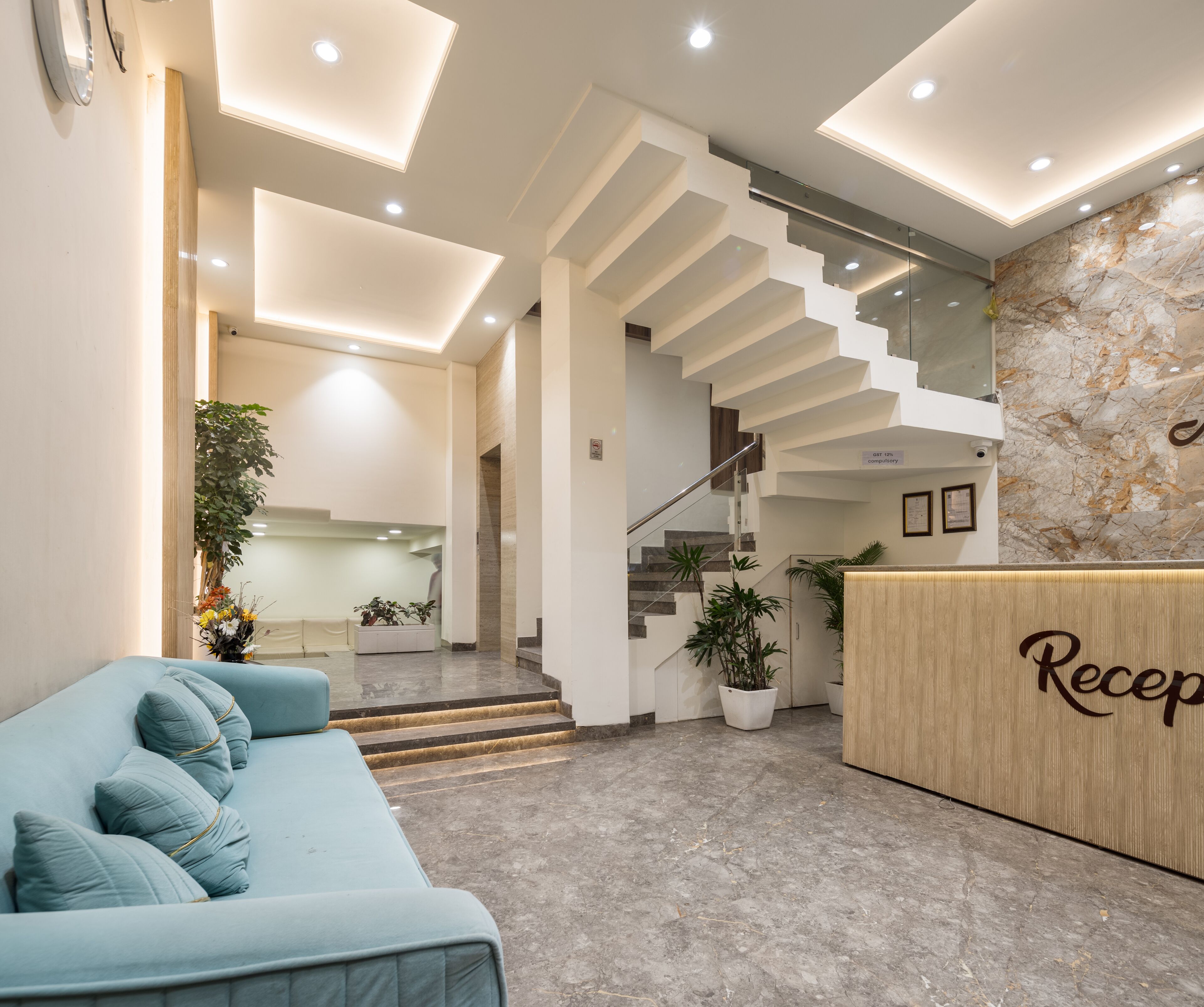 Un espace d’accueil moderne avec un canapé bleu clair, un comptoir d’accueil en bois et un escalier menant à l’étage supérieur.