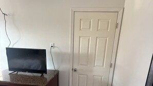 A room with a television on a dresser, a white door, and a wall-mounted picture frame.