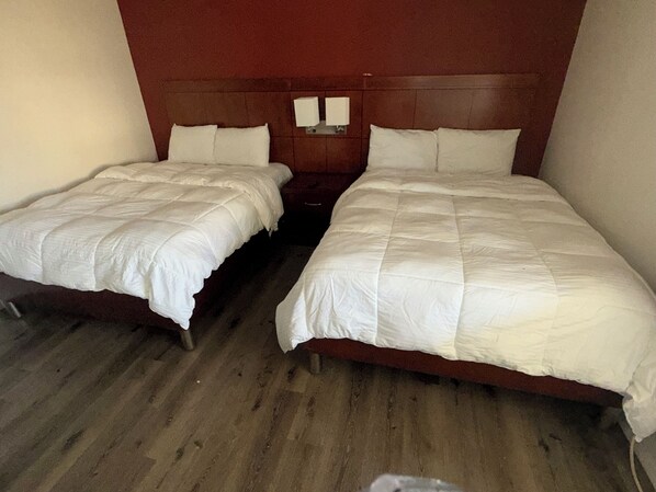 Two single beds with wooden frames and white bedding in a room with wooden flooring and a brown headboard.
