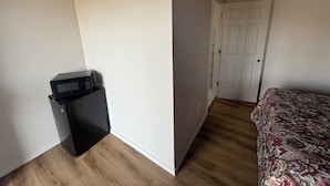 A room with a bed, a door, and a small black appliance against the wall.