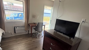 A hotel room with a wooden floor, a desk with a chair, a television on a stand, and a window with curtains.