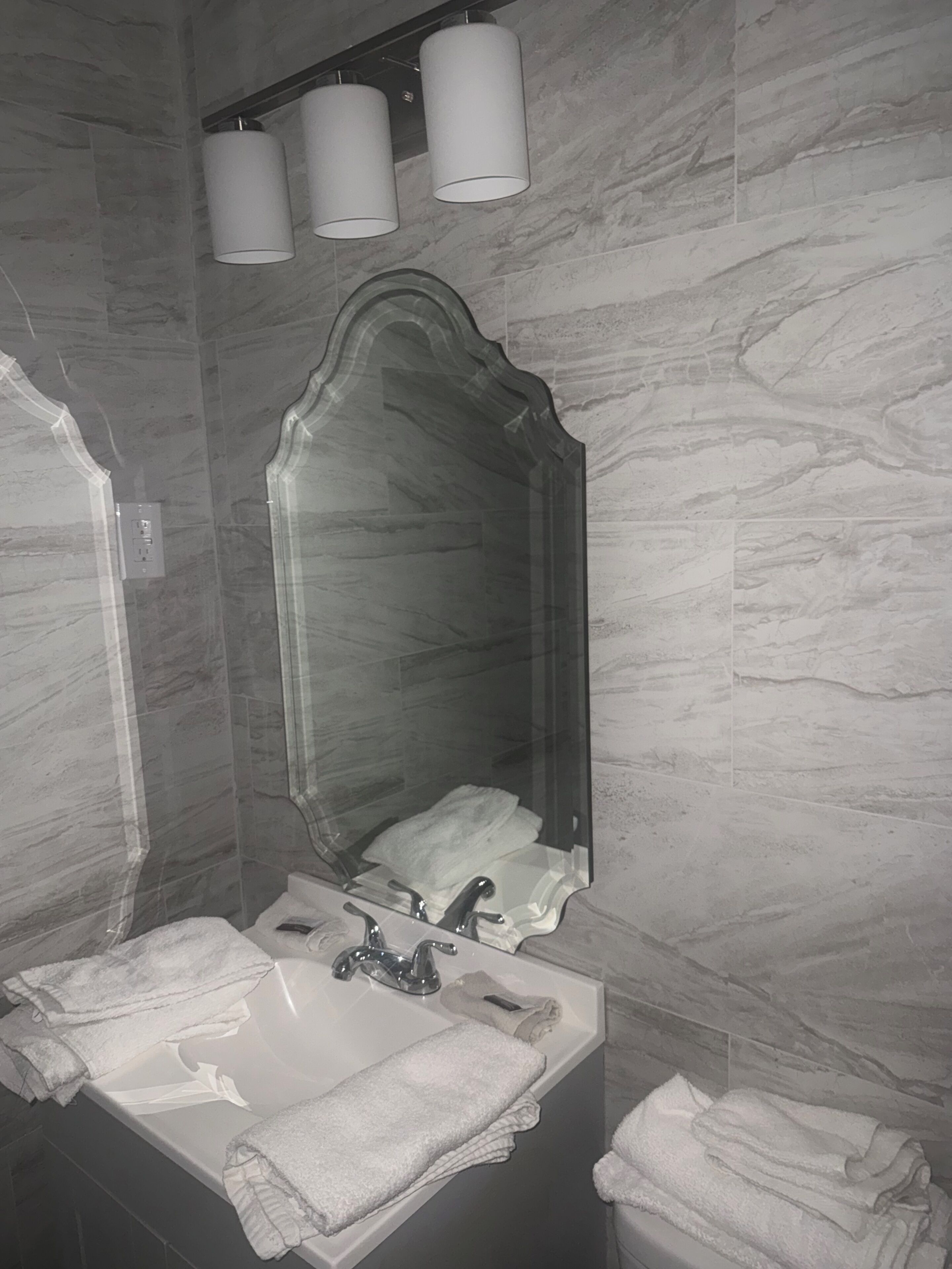 A bathroom with a marble wall, a sink with a mirror, and three wall-mounted lights.