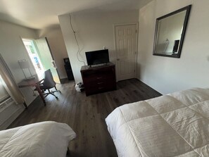 A bedroom with two beds, a desk with a chair, a dresser, a television, and a door.